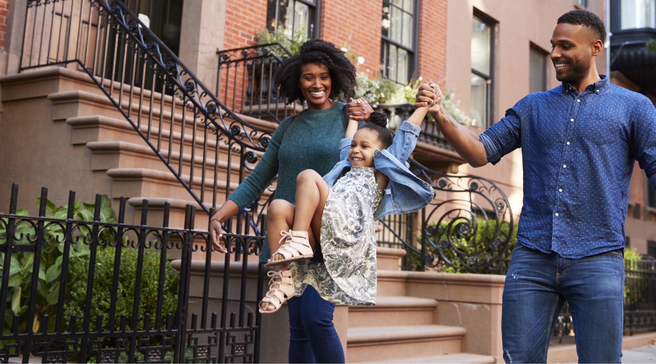 Mom and Dad swinging their daughter in front of apartment buildings